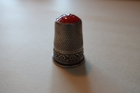 Fingerbøl af sølv fra gammel tid
Med en rød flus
Ikke  stemplet
Dekoreret med flot blomsterranke i sølvet