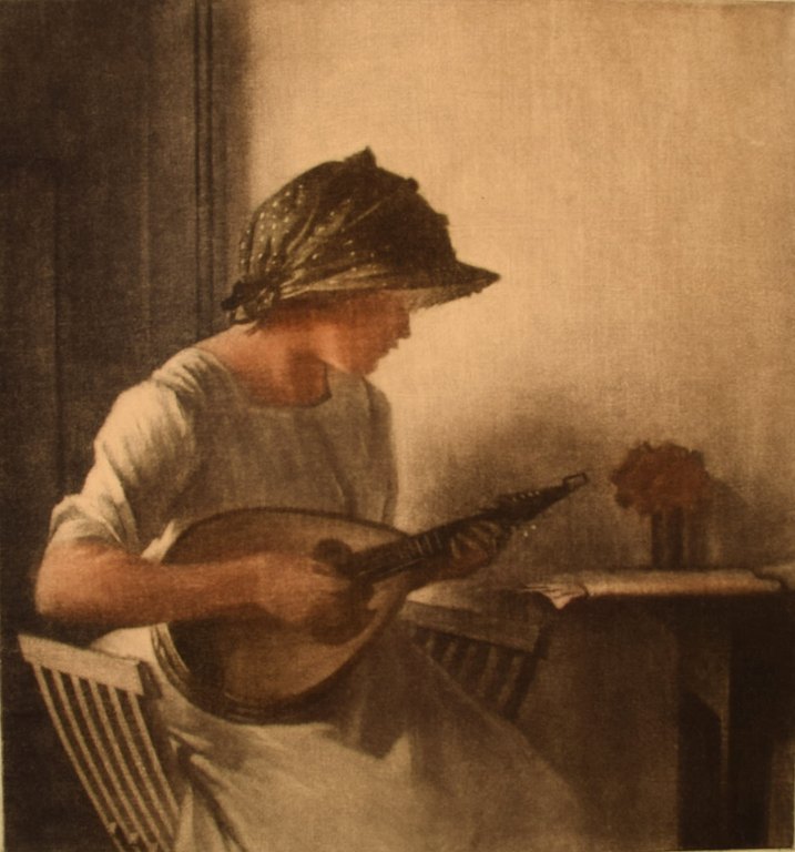 Peter Ilsted (1861-1933). Interiør med mandolinspillende ung kvinde. Mezzotinte 
i farver. 
