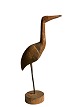 Skulpturel og dekorativ fugl udskåret af træ og stående på træfod.