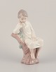 Lladro, Spanien. Porcelænsfigur af pige siddende på træstub.
