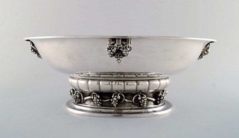 Georg Jensen stor og imponerende champagnekøler/drueskål af hammerslået 
sterlingsølv, prydet med hanke og ornamentik i form af drueklaser. Original 
mahognikasse fra Georg Jensen medfølger.
I flot stand.
