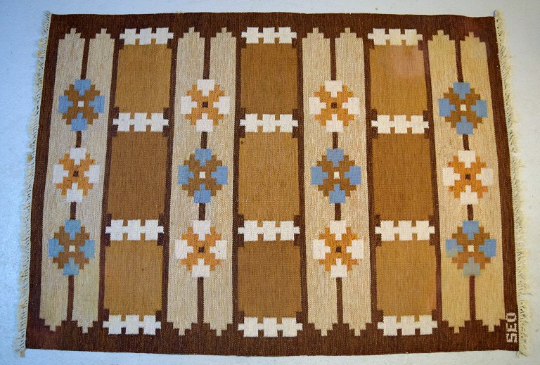 Svensk tekstildesigner. Stort håndvævet RÖLAKAN tæppe i ren uld med geometriske 
felter og rene linjer i brune, blå og sandfarvede nuancer. Midt 1900-tallet.
