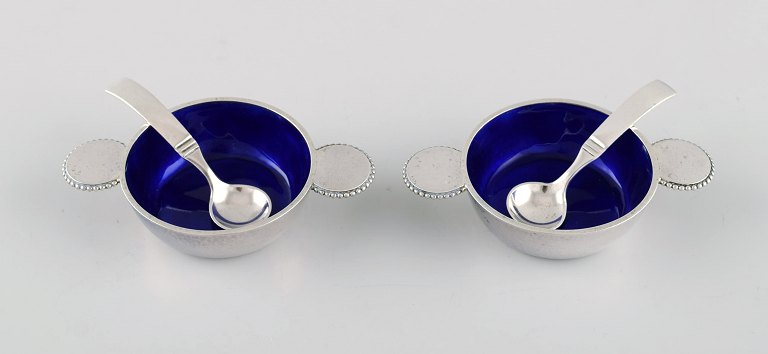 Two rare Evald Nielsen salt vessels in sterling silver with royal blue enamel 
and pearl border. Spoons by Danish silversmith. 1920/30