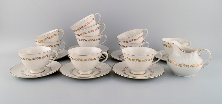 Royal Doulton, England. Twelve Fairfax teacups with saucers and a cream jug in 
porcelain with hand-painted flowers in gold. Mid-20th century.
