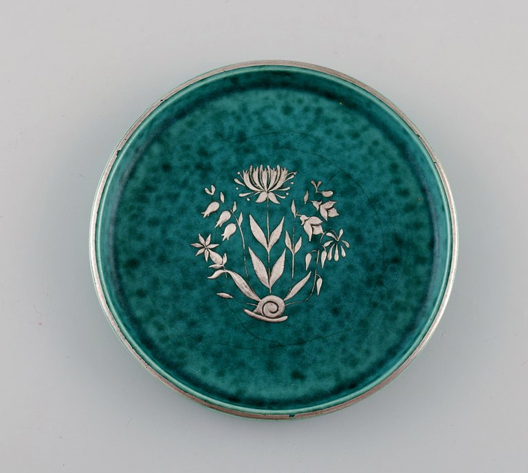 Wilhelm Kåge (1889-1960) for Gustavsberg. Rundt Argenta art deco fad i glaseret 
keramik. Smuk glasur i grønne nuancer med sølvindlæg i form blomst. Dateret 
1938.
