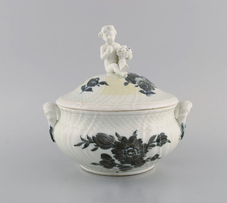 Tidlig Royal Copenhagen Blå Blomst Svejfet lågterrin i porcelæn med håndmalede 
blomster. Låg modelleret med frugtspisende putti. Ca. 1820.
