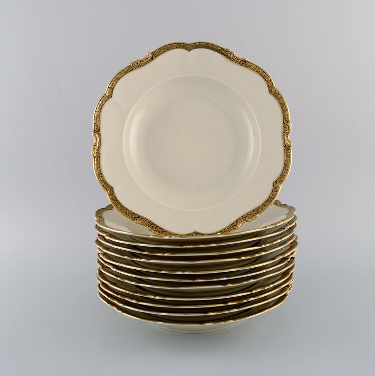 KPM, Berlin. Tolv Royal Ivory dybe tallerkener i cremefarvet porcelæn med 
gulddekoration. 1920
