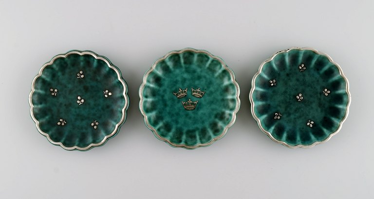 Wilhelm Kåge (1889-1960) for Gustavsberg. Three small Argenta dishes in glazed 
ceramics. Beautiful glaze in shades of green with silver inlay in the form of 
crowns and leaves. Mid-20th century.
