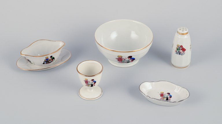 French childrens porcelain dinnerware consisting of a bowl, egg cup, pepper 
shaker, miniature sauce boat, and a small oval dish. Motifs of children at play.