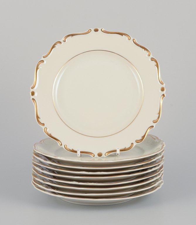 KPM, Poland. A set of nine cream-colored porcelain plates with gold decoration.