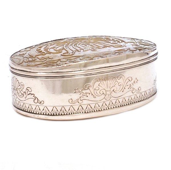 Stor oval tabatiere udført i sølv af Poul Søren Bay, København, ca. år 1750. Låg og bund prydet med perlemor. Låg med dybt skåret spejlmonogram under engle og krone. H: 5cm. L: 11,6cm. V: 193gr